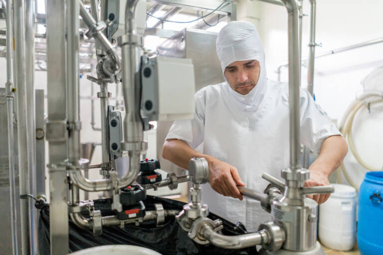 operator in sanitary protective gear managing stainless steel processing equipment in a modern food production facility