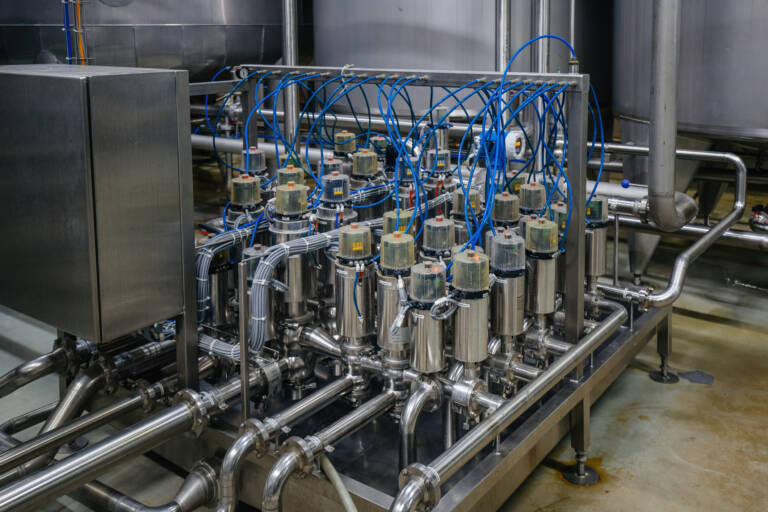 a dense matrix of stainless‑steel mixproof separation valves connected by piping and blue control lines inside a sanitary processing facility