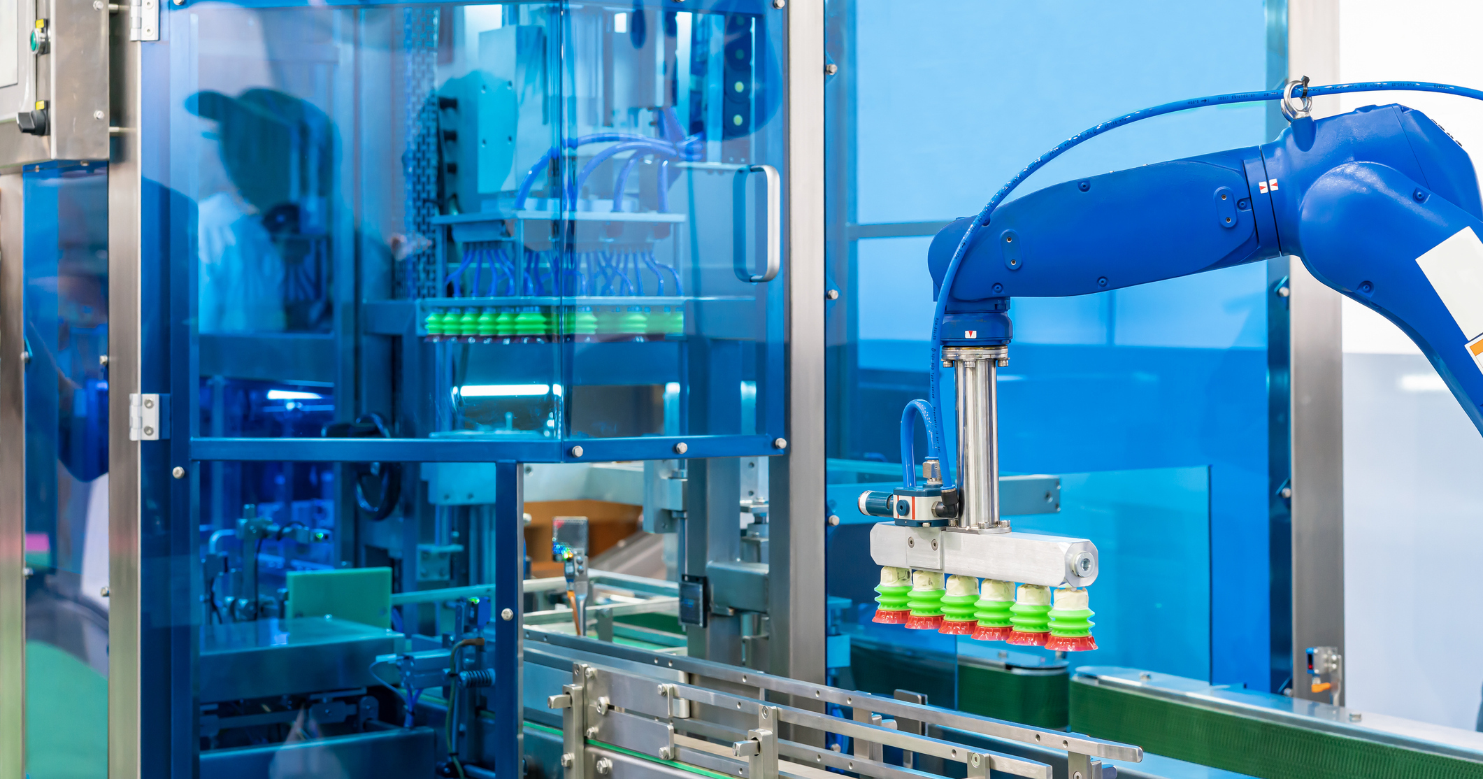 automated robotic arm with suction gripper moving bottles along a conveyor inside a protected industrial production cell