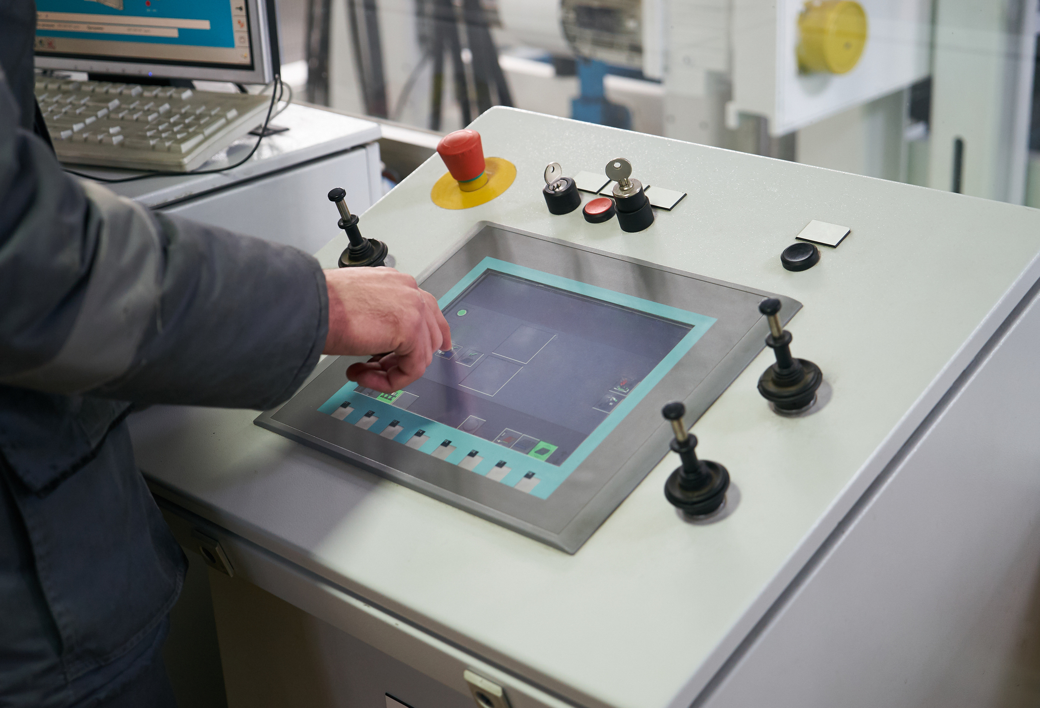 operator using a touchscreen industrial control panel with buttons switches and an emergency stop in a modern manufacturing environment